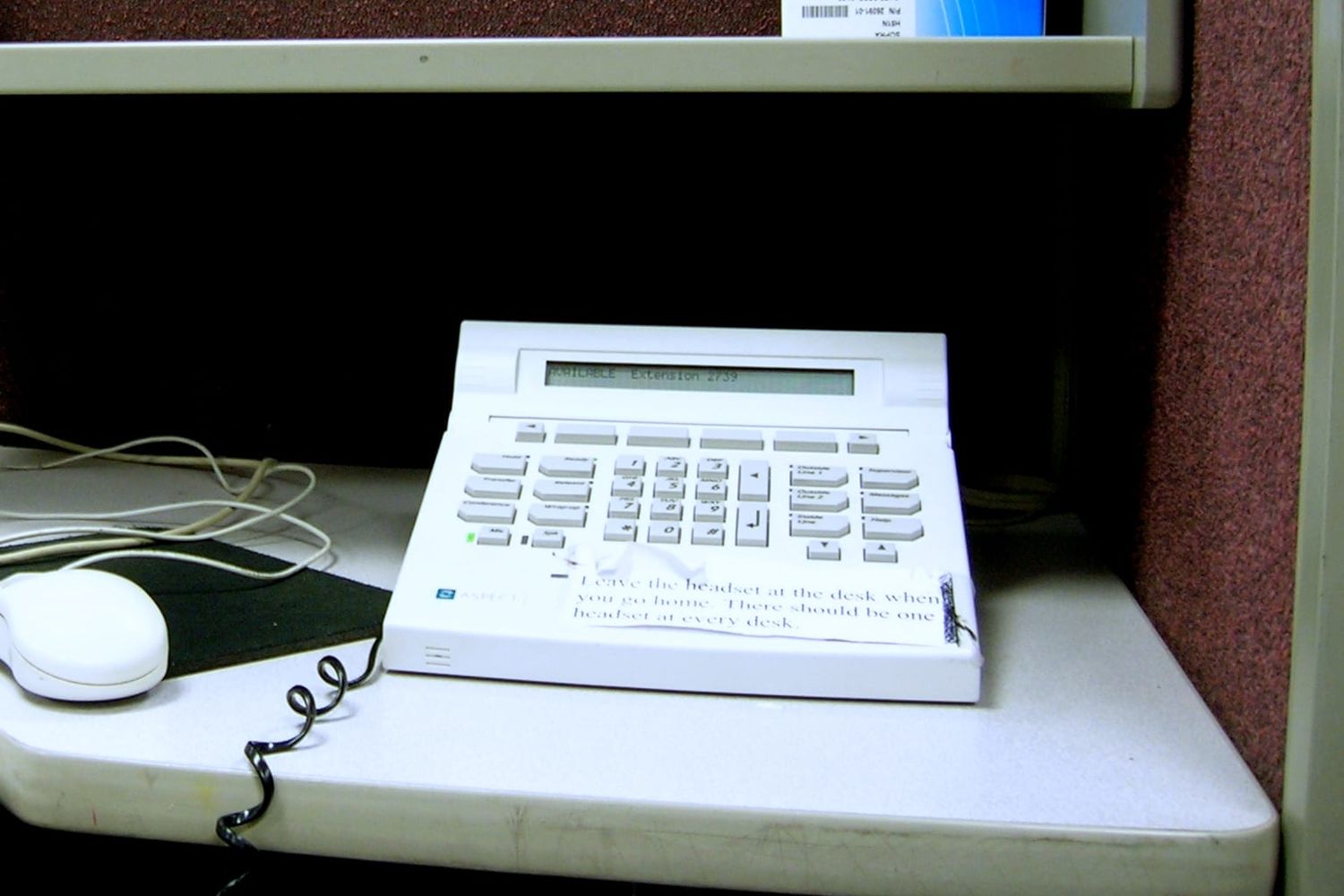 Weißes Callcenter-Telefon mit Display auf einem grauen Schreibtisch im Großraumbüro