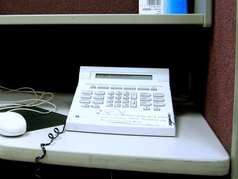Weißes Callcenter-Telefon mit Display auf einem grauen Schreibtisch im Großraumbüro