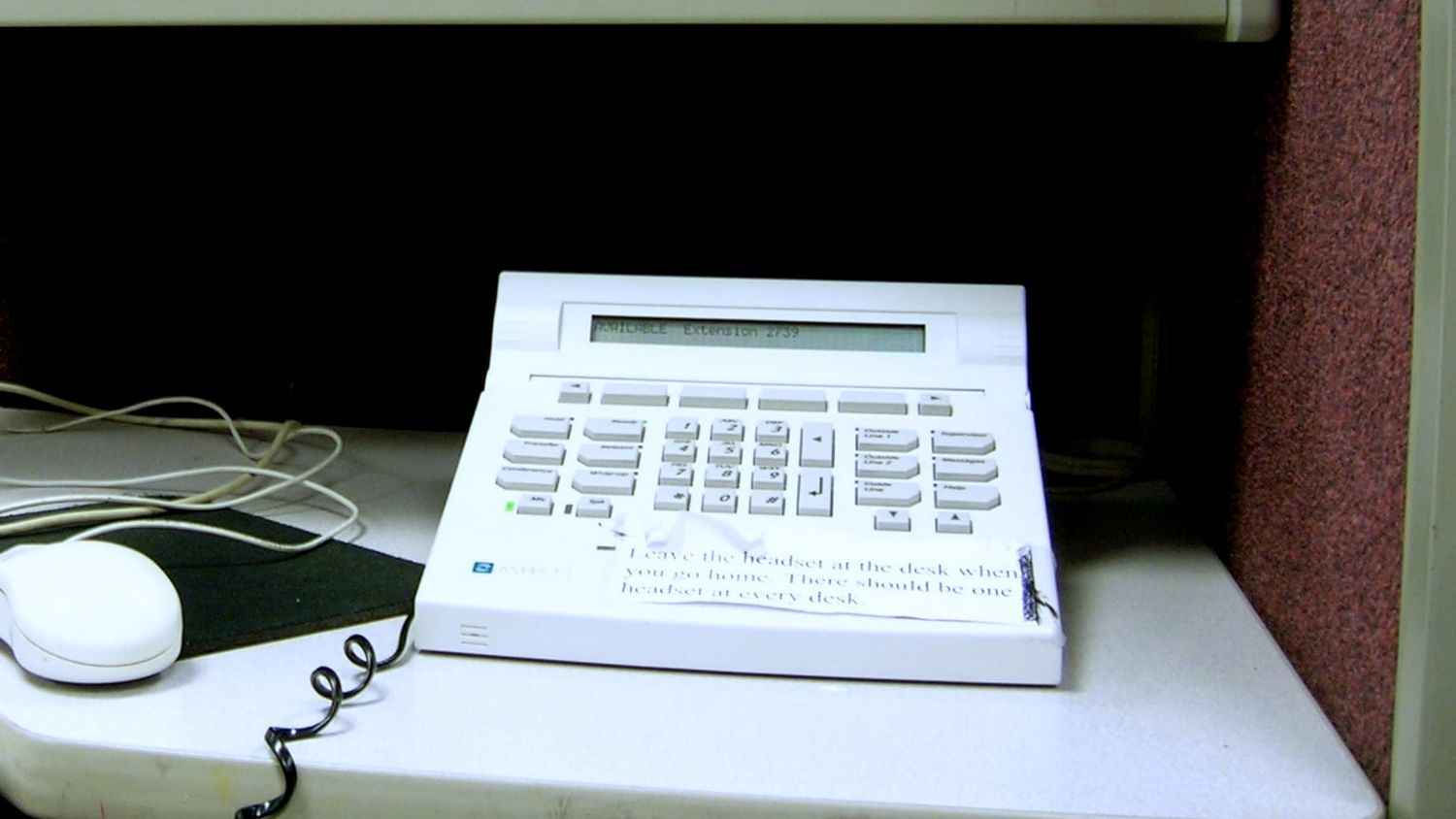 Weißes Callcenter-Telefon mit Display auf einem grauen Schreibtisch im Großraumbüro
