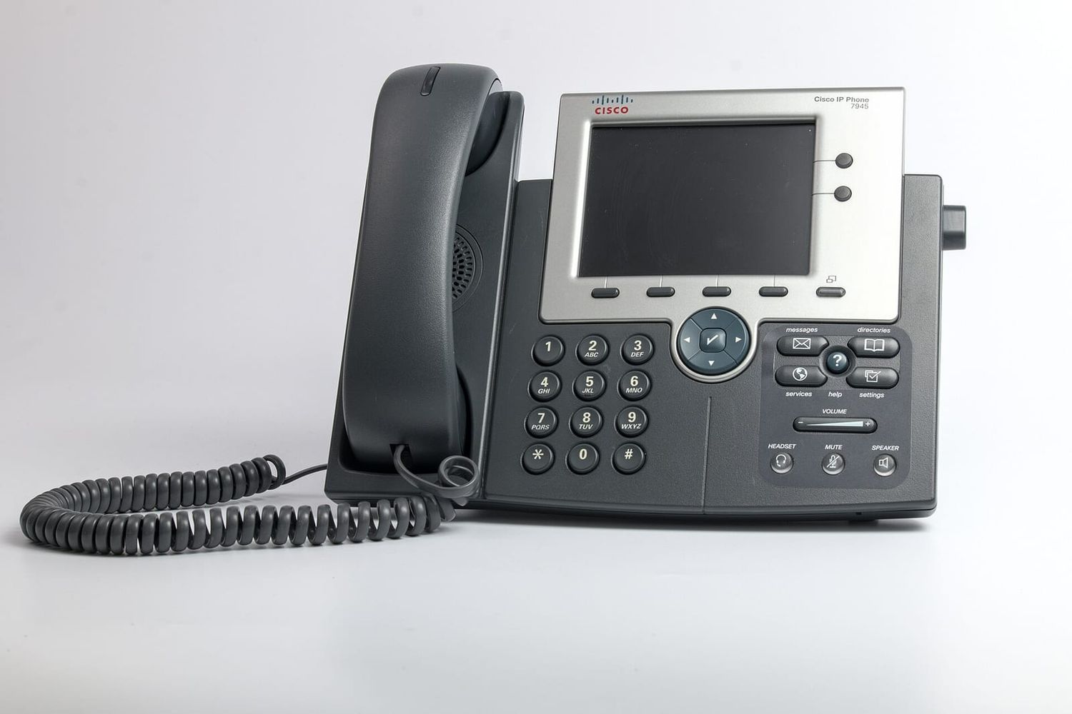 Graues IP-Tischtelefon mit Farbdisplay und Spiralkabel vor hellem Hintergrund