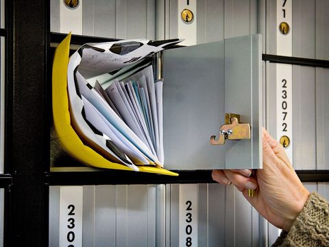 Hand öffnet ein Postfach voller Briefe und Umschläge in einer Postfachanlage