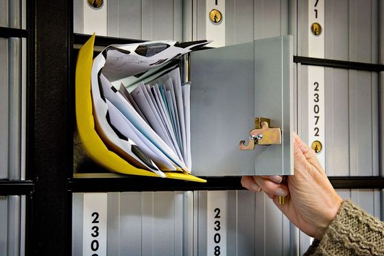 Hand öffnet ein Postfach voller Briefe und Umschläge in einer Postfachanlage