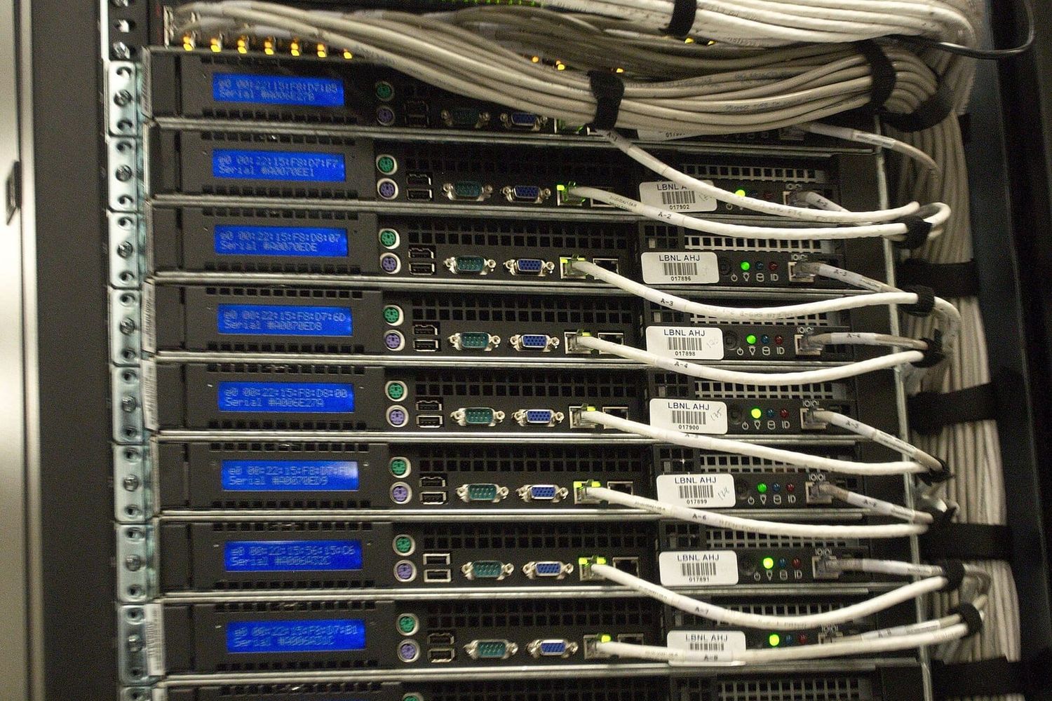 Serverschrank mit gestapelten Rechnern, blauen Displays und gebündelten Netzwerkkabeln