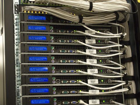 Serverschrank mit gestapelten Rechnern, blauen Displays und gebündelten Netzwerkkabeln